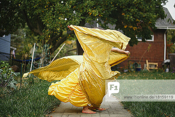 Ein Kind in einem ausgefallenen Kleid wirbelt in langen goldenen Umhang draußen