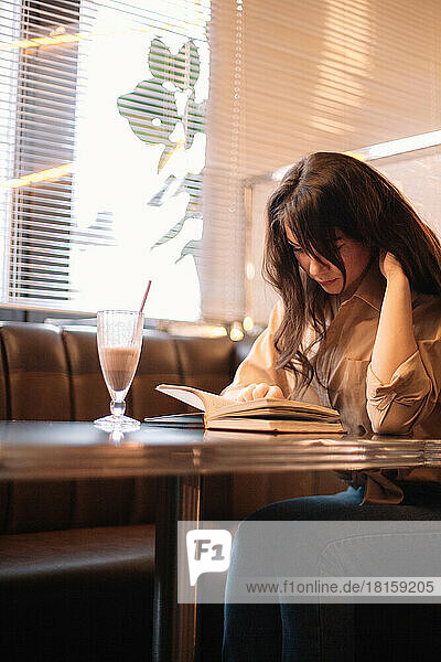 Junge Frau  die in einem Café sitzt und ein Buch liest