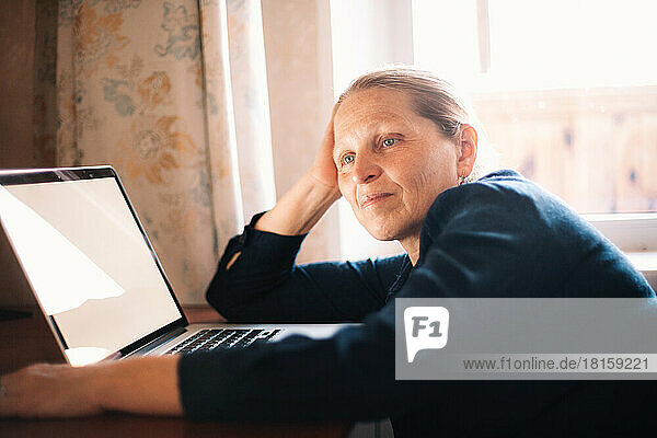 Nachdenkliche Frau am Schreibtisch sitzend vor einem Laptop-Computer zu Hause