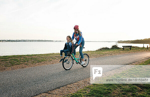 mother and daughter cycling together on a hire bike at the beach