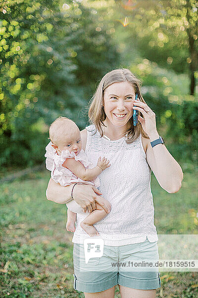Mother talks on phone outside while holding infant daughter.