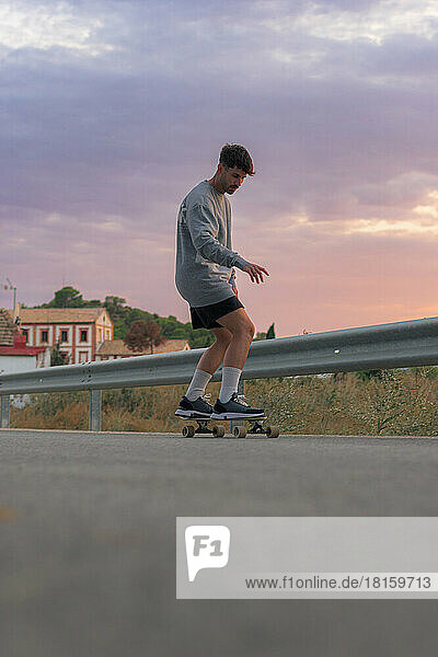Young man on a skateboard on the road at sunset