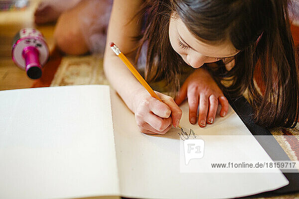 Close-up of child carefully drawing with pencil in sketchbook
