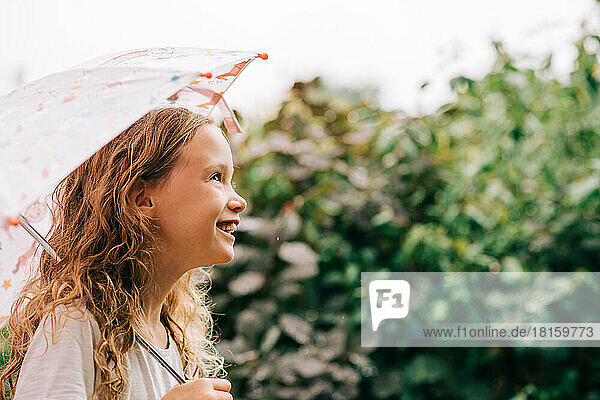lachendes Kind  das draußen im Regen einen Regenschirm hält
