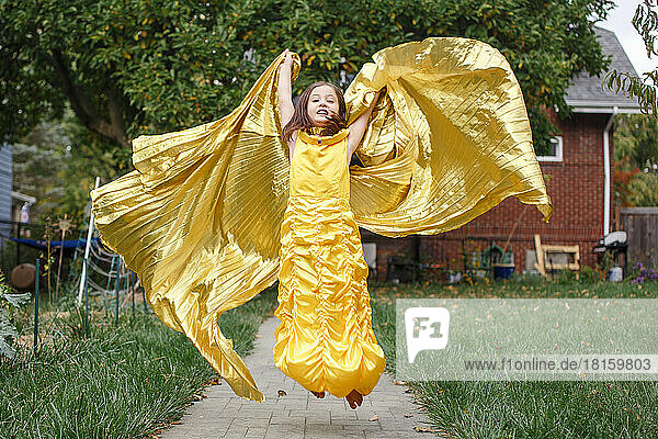 Ein engelhaftes kleines Mädchen in goldenem Kleid und langem Umhang springt in die Luft