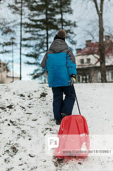 Ein Kind mit einem roten Schlitten klettert auf eine Schneerutsche.