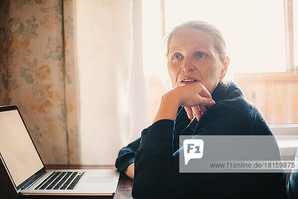 Nachdenkliche reife Frau sitzt am Laptop und arbeitet zu Hause