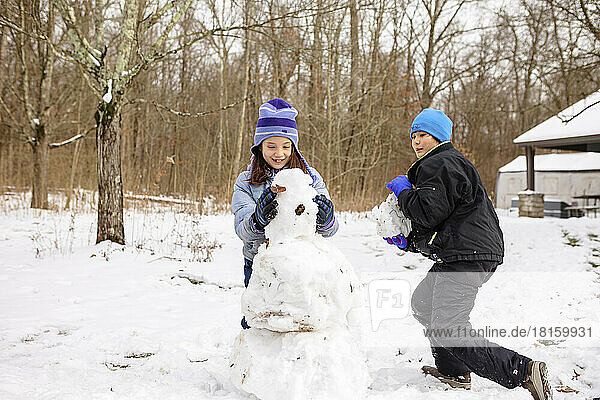 Two happy children build snowman together in winter