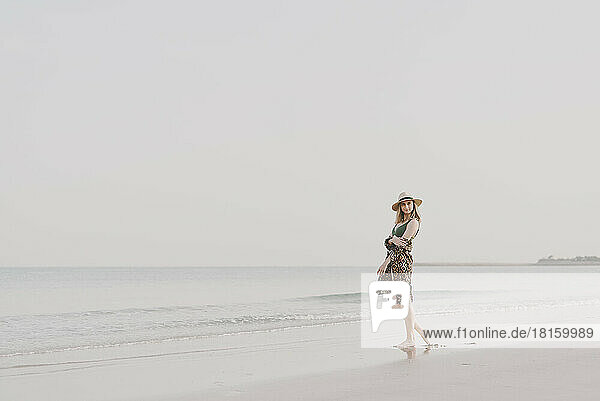 Junge Frau in Strandkleidung und Hut am Strand stehend