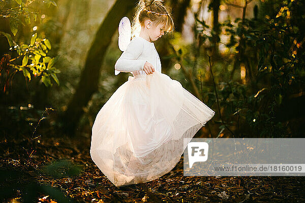 Mädchenkind wirbelt in goldenem Licht im Wald in Engelskostüm