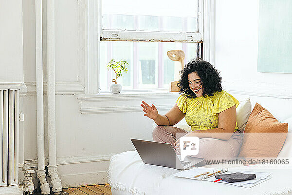 Happy businesswoman waving on video call over laptop in office studio