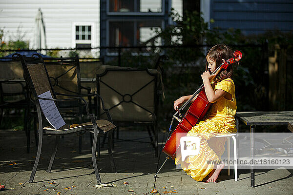 Seitenansicht eines konzentrierten  barfüßigen Mädchens  das draußen im Kostüm Cello spielt