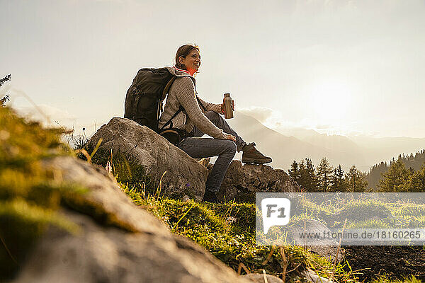 Smiling woman holding water bottle sitting on rock