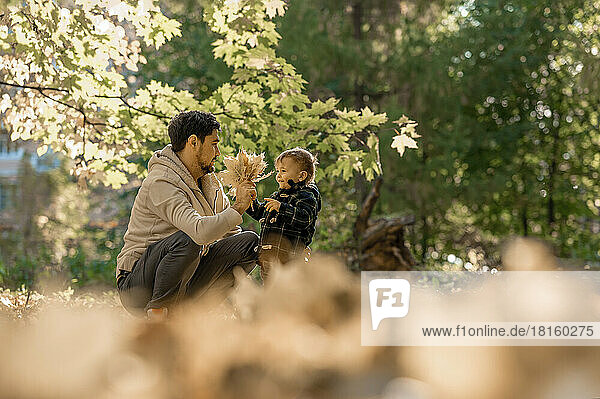 Vater und Sohn spielen mit Herbstblättern im Park