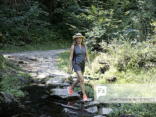 Smiling senior woman wearing hat walking on rocks in forest