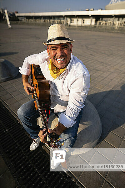 Happy guitarist wearing hat playing guitar on sunny day