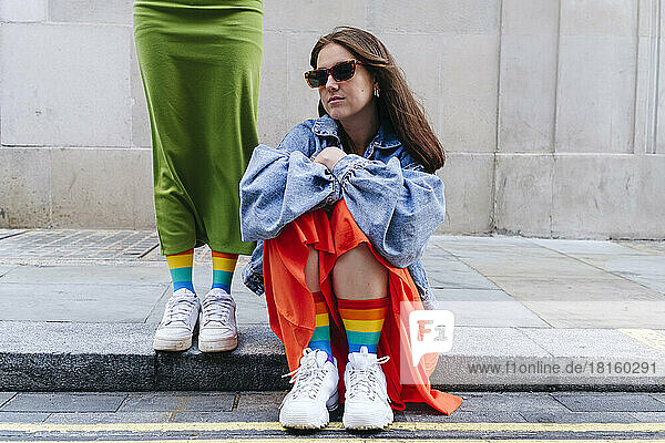 Woman wearing sunglasses sitting by lesbian friend standing on footpath