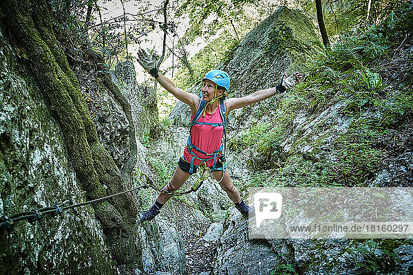 Woman with arms outstretched climbing mountain in forest