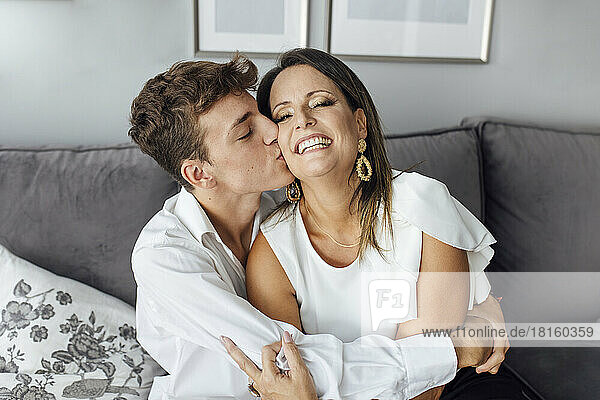 Teenage boy kissing mother on cheek at home