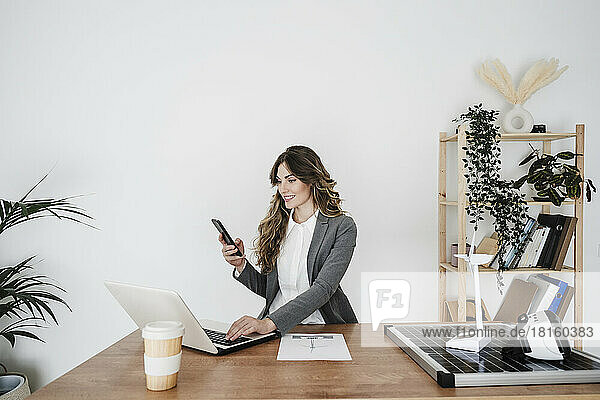 Young female engineer working in modern office sitting at desk using smartphone