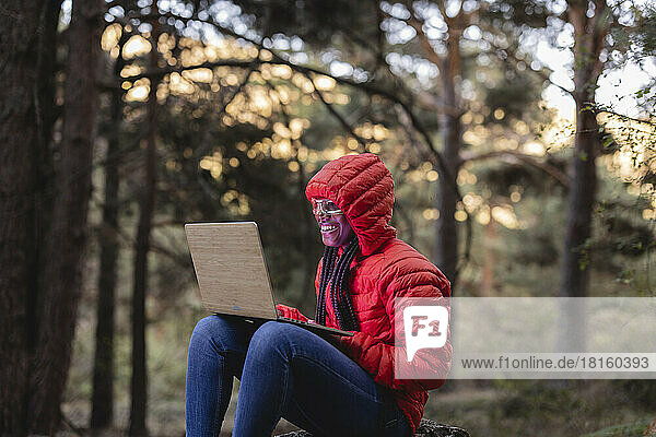 Happy woman with smart glasses working on laptop in forest