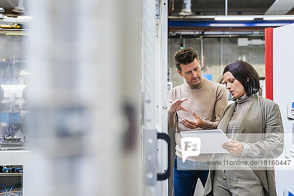 Businesswoman holding tablet PC discussing about machine in industry
