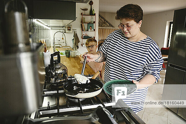 Woman making omelet with son standing by kitchen counter at home