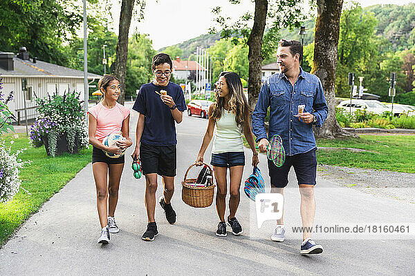 Happy multiracial family with picnic supplies walking on road