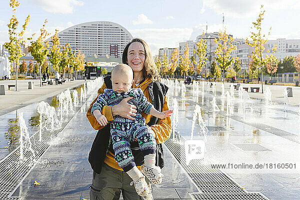 Happy mother and son enjoying with each other amidst fountains at urban park