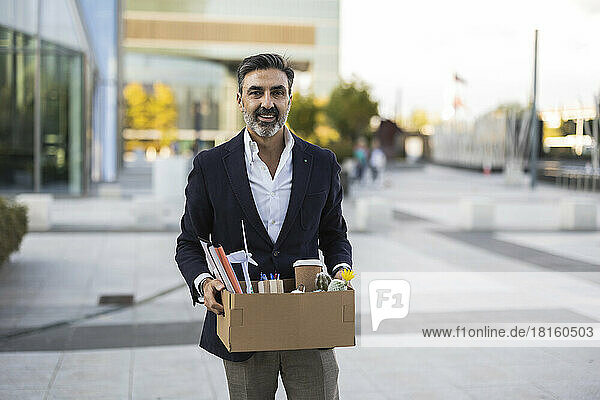 Smiling businessman holding box with office supplies