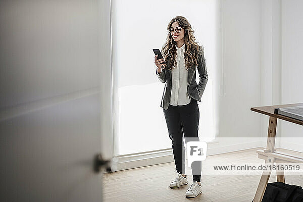 Junge Geschäftsfrau steht mit Smartphone im Büro