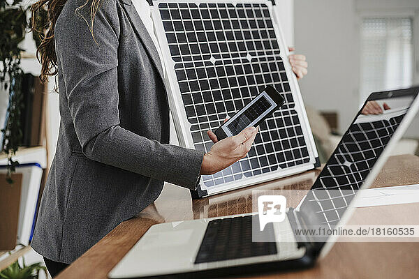 Modern businesswoman with smartphone using portable solar module in office