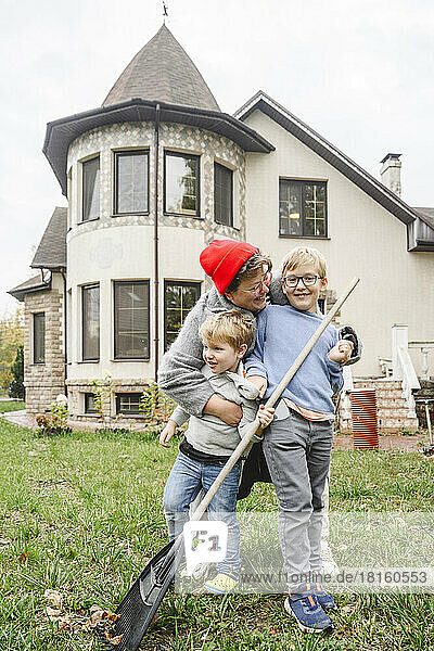 Happy mother hugging boys standing in front of house at back yard