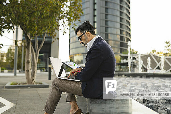 Businessman using laptop sitting on wall