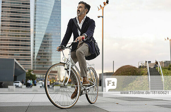 Businessman enjoying riding bicycle on footpath