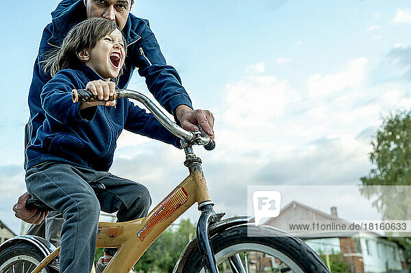 Fröhlicher Junge  der vom Vater Fahrrad fährt