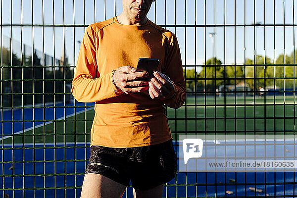 Sportler hält Mobiltelefon vor Zaun