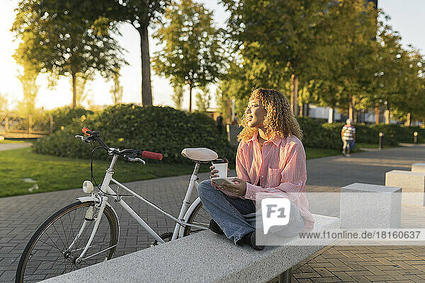 Thoughtful woman with disposable coffee cup sitting on bench