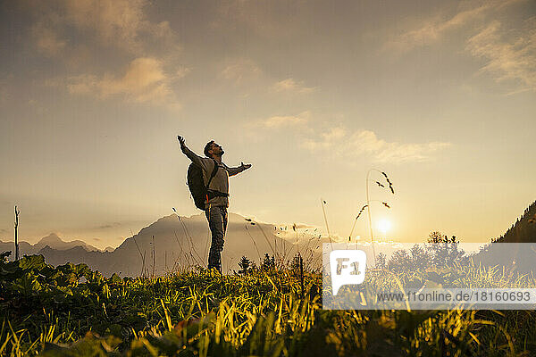 Mature man standing with arms outstretched on top of mountain at sunset