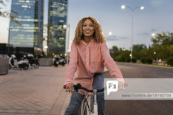 Smiling blond woman riding bicycle on road in city