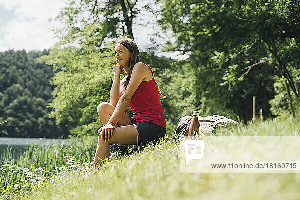 Smiling woman with hand on chin sitting on grass