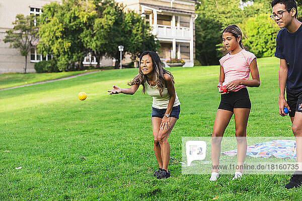 Woman throwing ball by son and daughter standing on grass