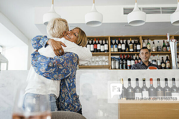 Happy mature businesswoman hugging friend at restaurant