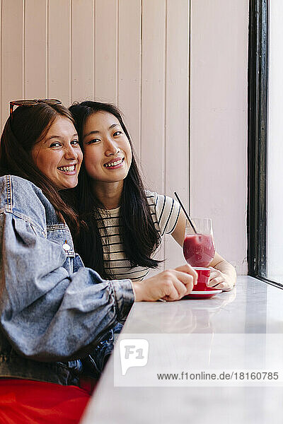 Smiling lesbian couple with drinks on table at cafe