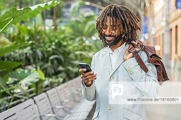 Smiling businessman holding shoulder bag using smart phone