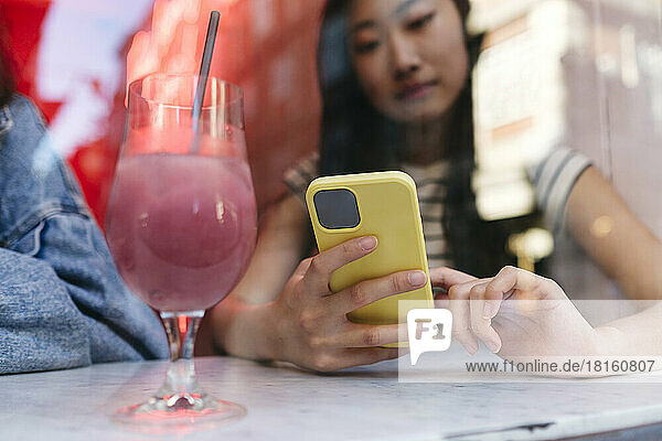 Woman using smart phone by drink glass on table at cafe