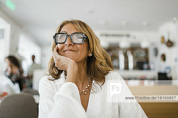 Thoughtful mature businesswoman with hand on chin sitting in restaurant