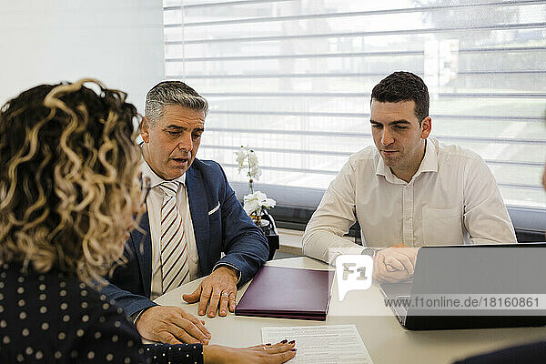 Mature businesswoman discussing over document with colleagues at desk
