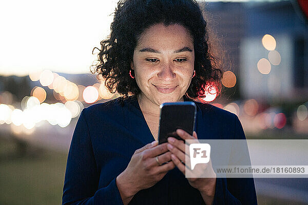 Smiling businesswoman using mobile phone at dusk