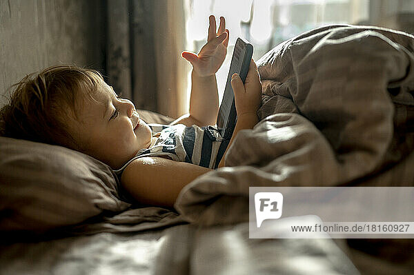 Baby boy using mobile phone in bed at home